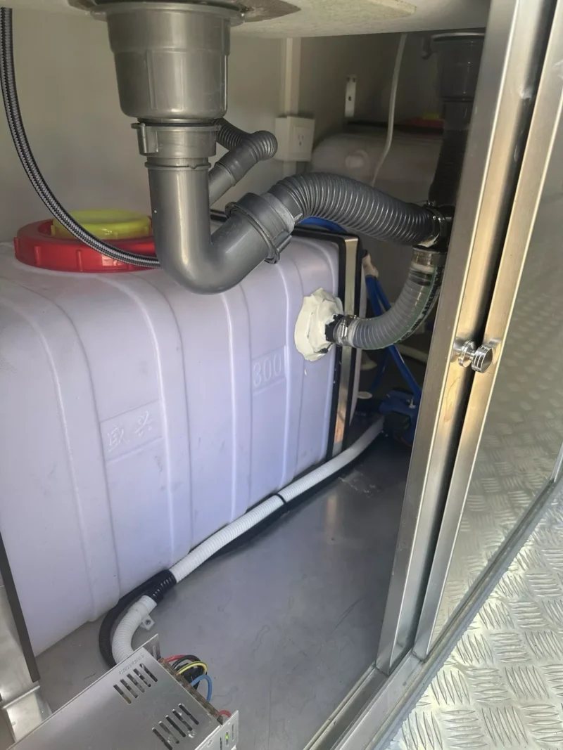 14 ft Food Trailer – Red Finish – Plumbing pipes and a large white water tank located under the sink