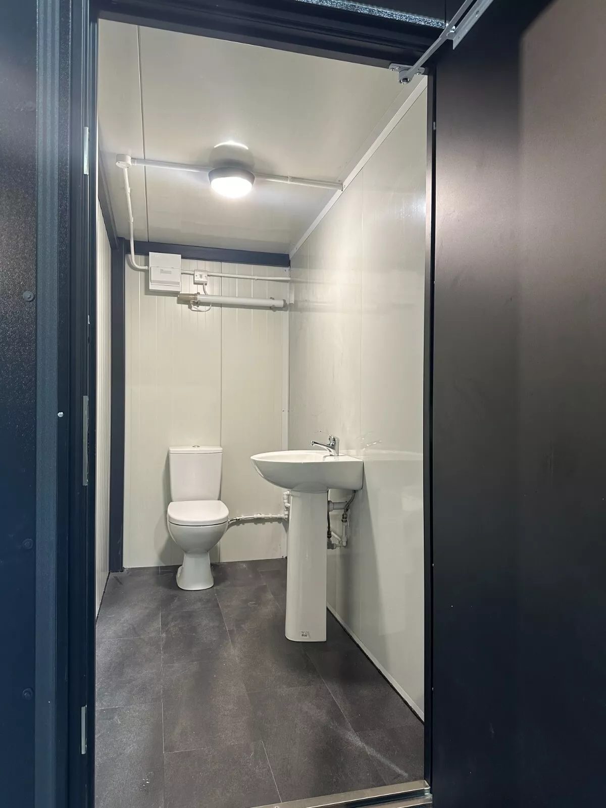Custom Shipping Container Restroom – Three Private Compartments – compact restroom with toilet and pedestal sink through doorway