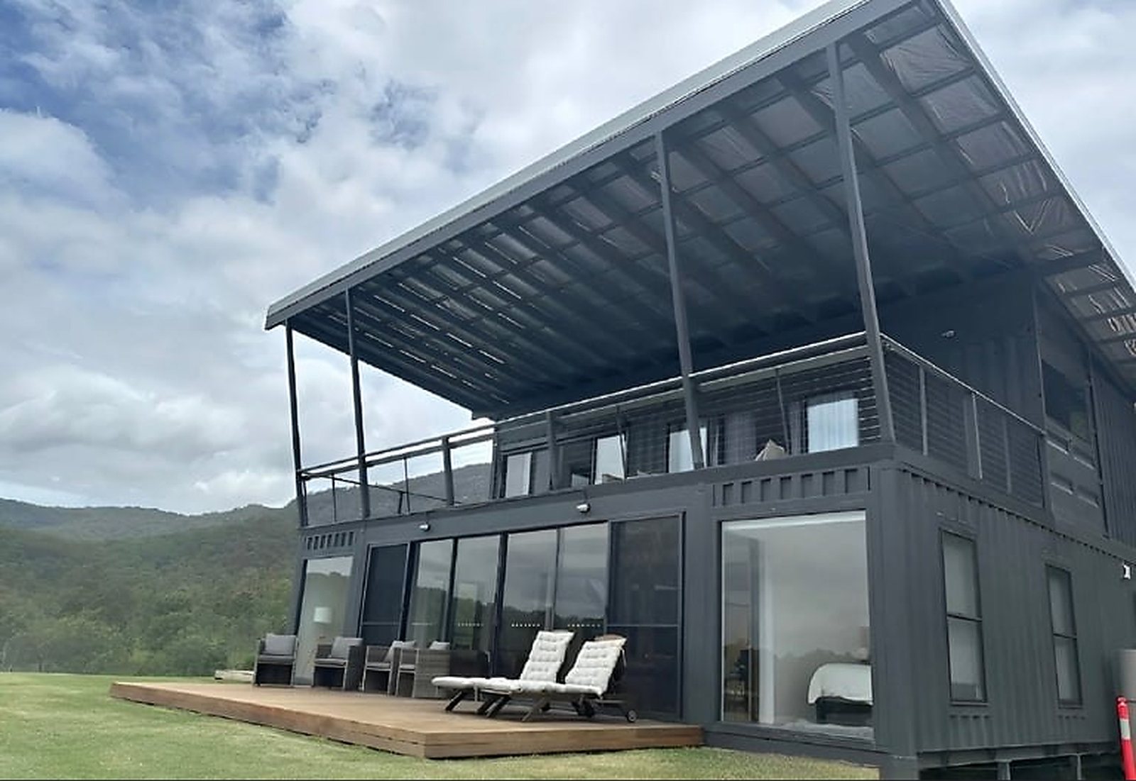 3-Bedroom Two-Story Container Home – Upper Terrace & Patio – Charcoal steel exterior with a wraparound timber patio and a wide cantilevered roof over the upper terrace