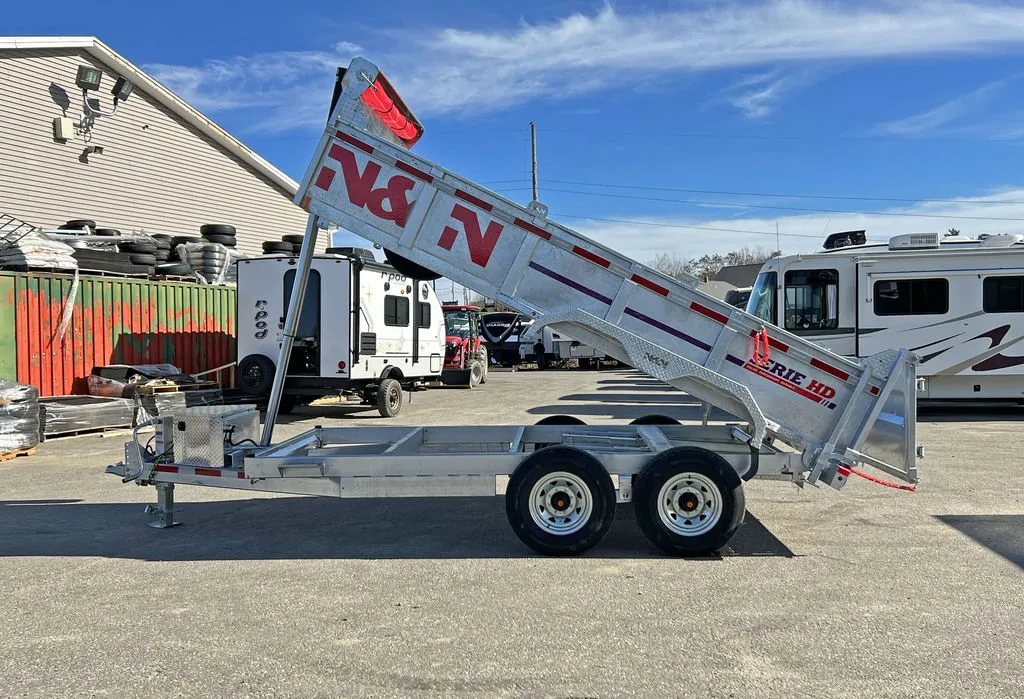 2024 N&N Trailers 14 ft Dump – Galvanized Steel – Side view of the trailer with the bed raised against a building background