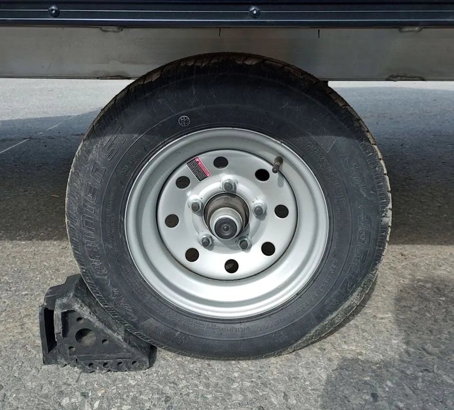 Mission Trailers Aluminum Crossover – Rear Canopy – Close-up of a trailer wheel and tire with a black wheel chock
