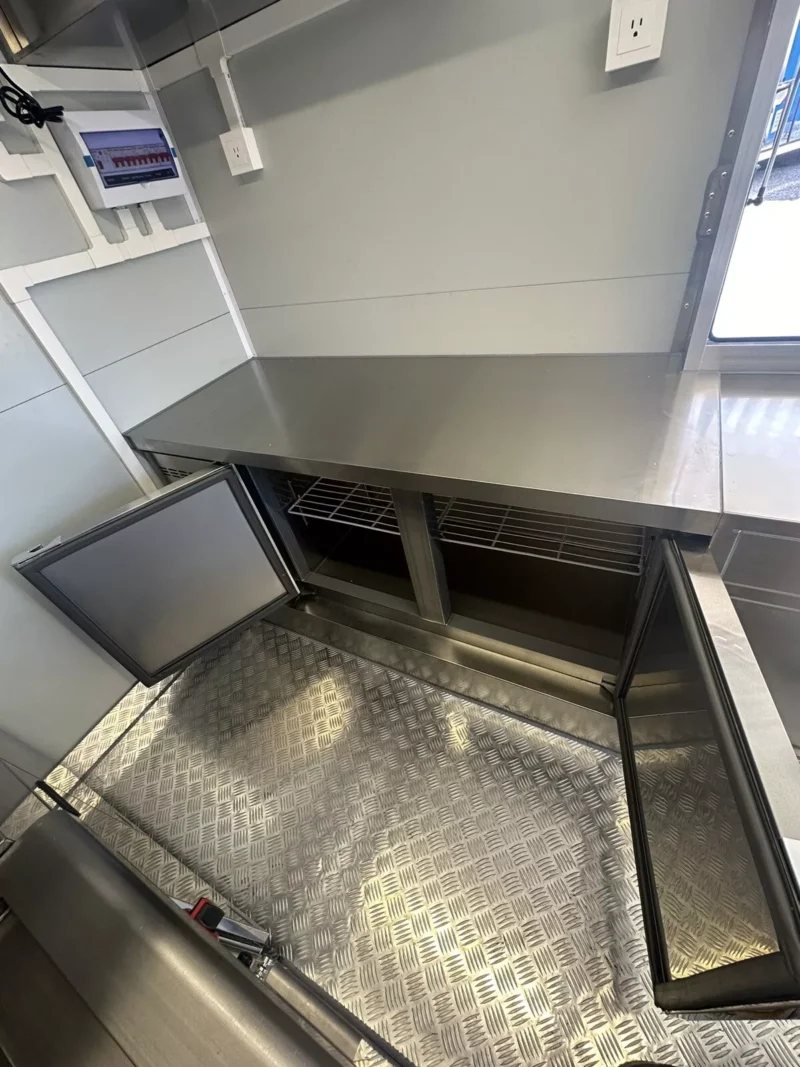 14 ft Food Trailer – Red Finish – Open under-counter refrigeration unit showing wire racks and diamond plate floor