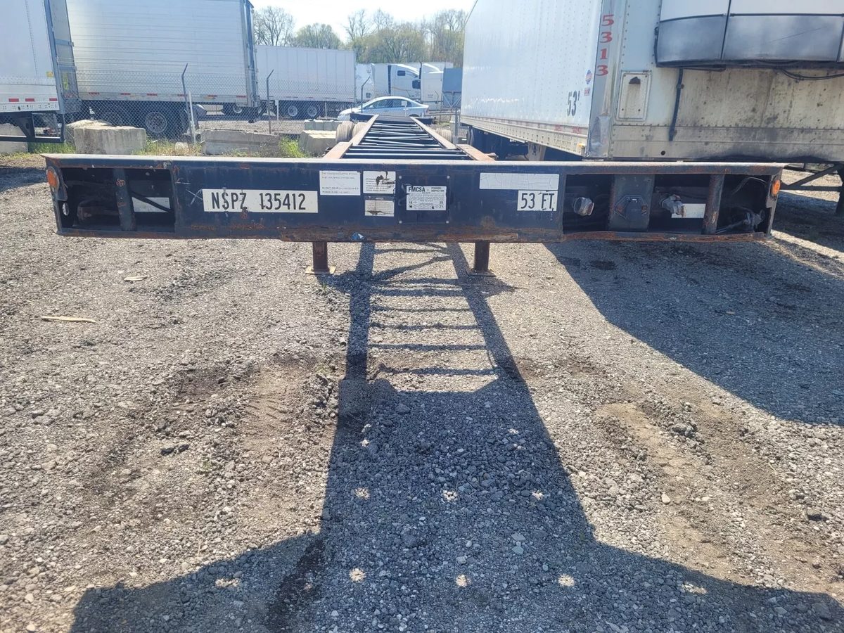 53ft Used Container Chassis – 2011, Spring Suspension – end-on view of empty chassis in crowded trailer yard