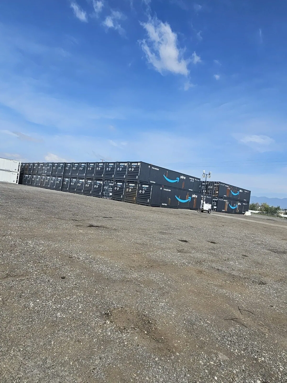 53ft High Cube Shipping Container – Used, Multi-Trip – Rows of dark shipping containers stacked in a gravel yard