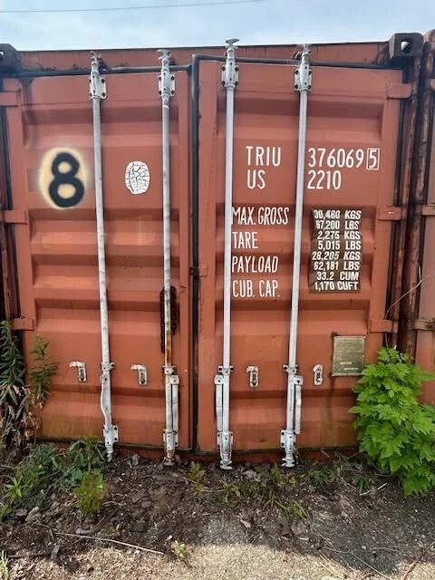 20ft Used Shipping Container – Double Cargo Doors – closed cargo doors on weathered container with surrounding weeds