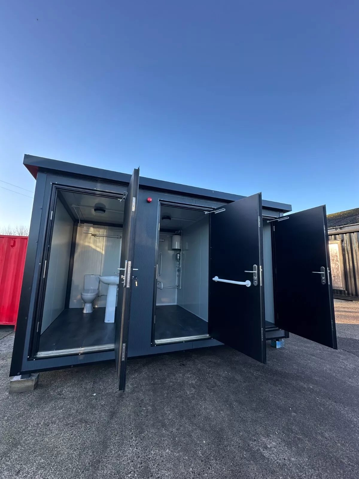 Custom Shipping Container Restroom – Three Private Compartments – Three open restroom doors revealing toilet and washbasin