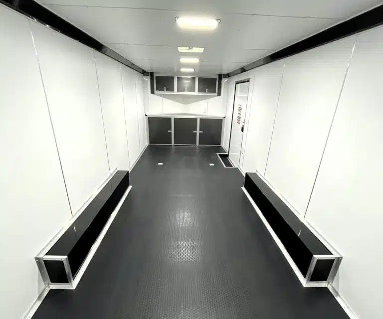 2025 Millennium 24 ft Car Hauler – Charcoal – Finished white interior looking towards the front showing cabinets and side door
