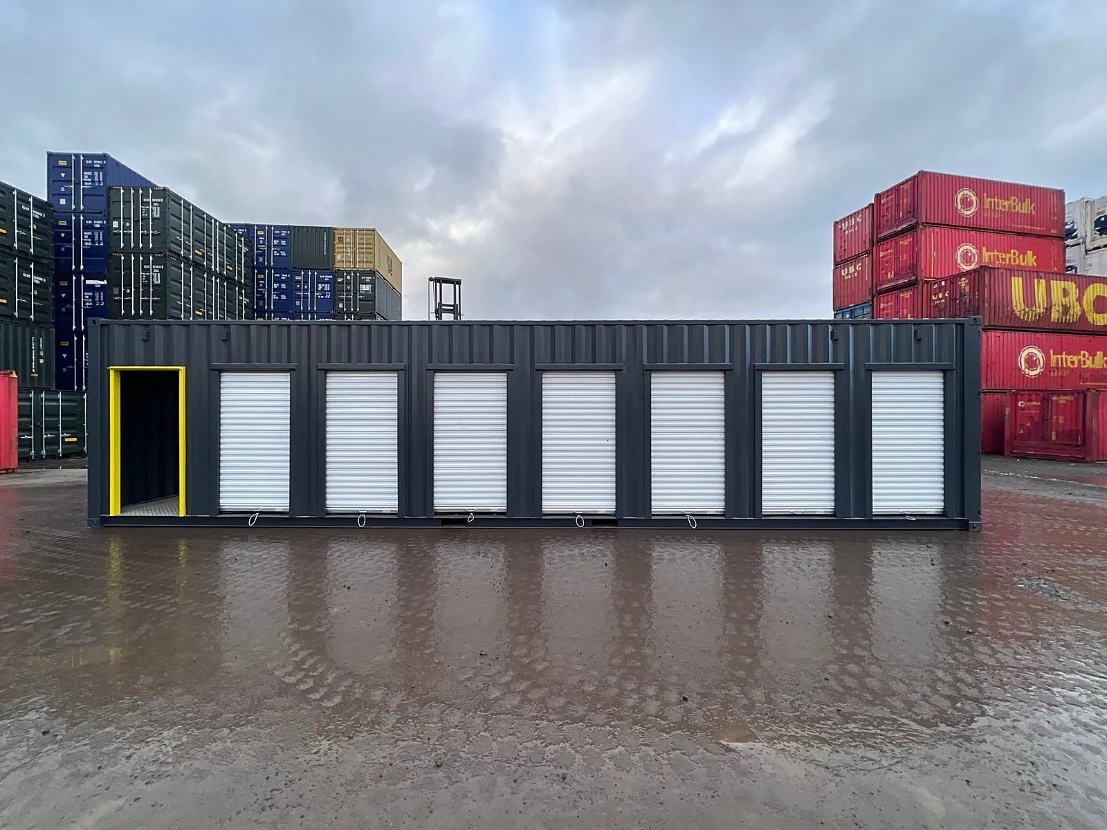 40ft High Cube Storage Container – Seven Lockable Bays – Front exterior with seven white shutters and open personnel doorway