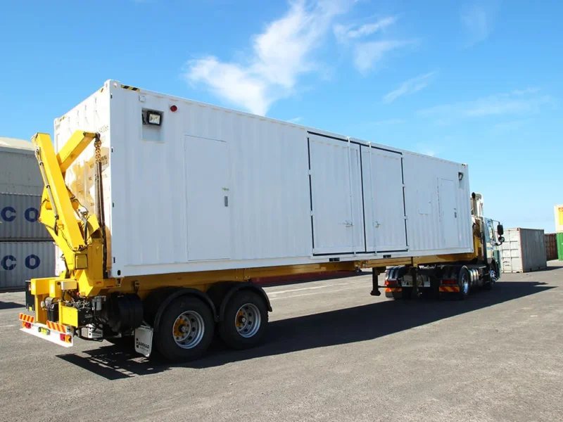 20 ft Switch Room Container – Insulated Panels – White specialty container mounted on a yellow transport trailer under a clear blue sky
