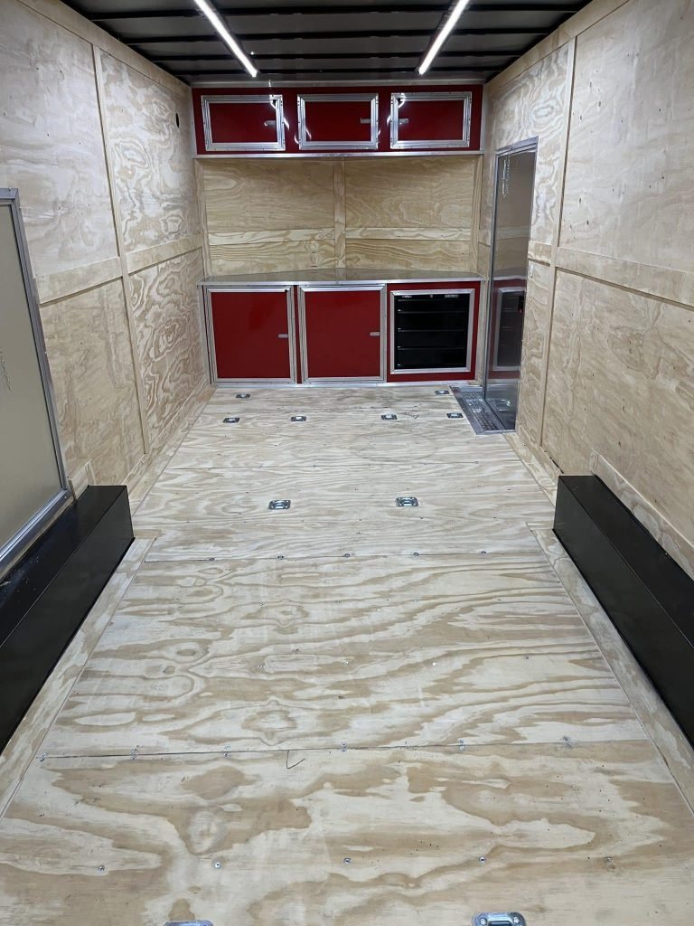 2026 Millennium 24 ft Car Hauler – Red, Econo-Max – Interior view facing forward showing red cabinets, toolbox, and plywood interior finishing