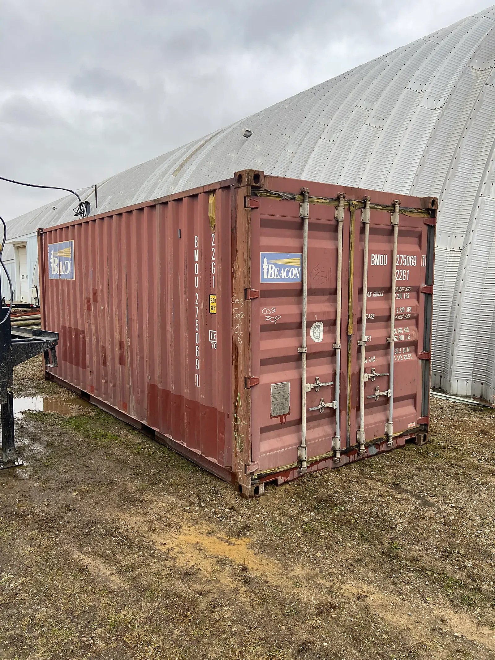 20ft Used Shipping Container – Double Cargo Doors – Weathered red shipping container with closed double cargo doors beside a corrugated metal building