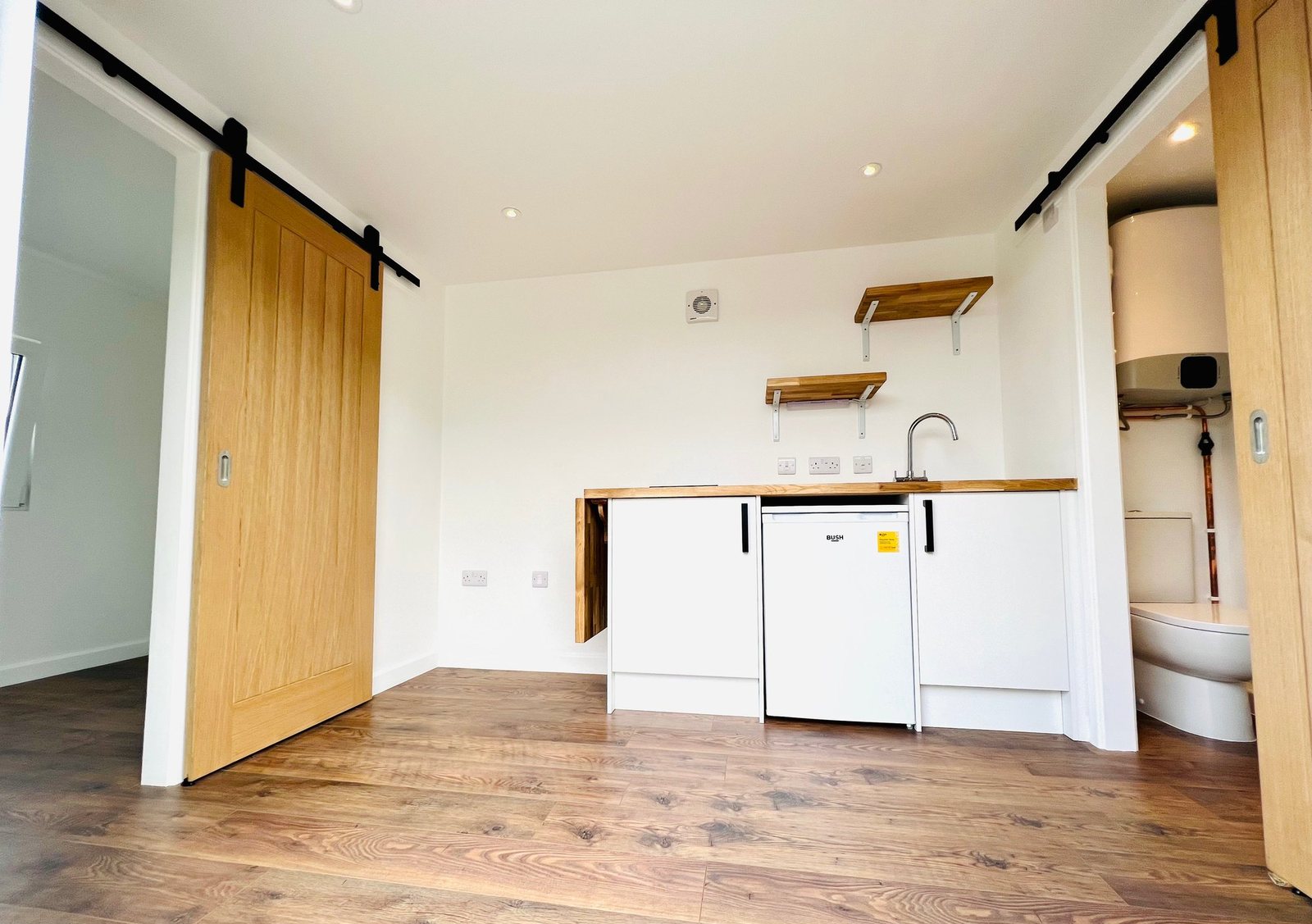 20ft Container Home – One Bed Box, 1 Bedroom – The interior of this refurbished 20ft container home features space-saving cabinetry and a high-quality wood laminate floor
