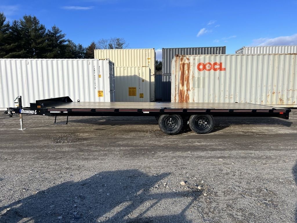 2024 Diamond C 22 ft Deckover Trailer – Slide-In Ramps – Full side profile view of the black deckover trailer against storage containers