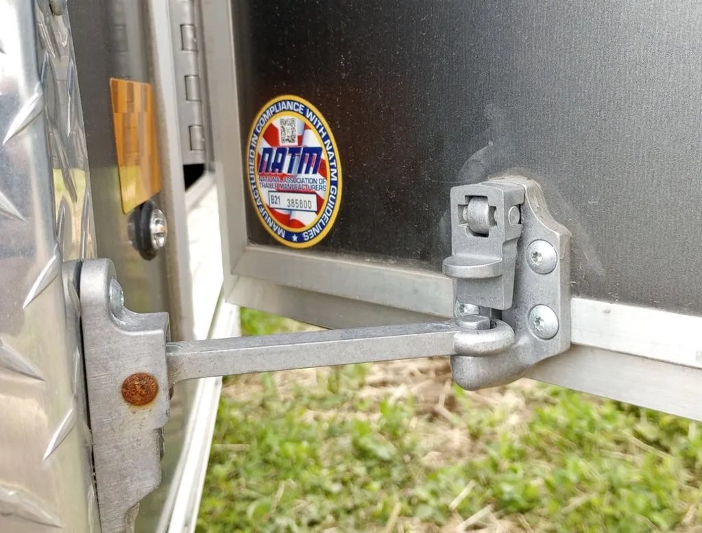 2022 Sno Pro Trailers Hybrid 2.0 – Charcoal Snowmobile Trailer – Detailed view of a metal trailer door hinge and a safety sticker
