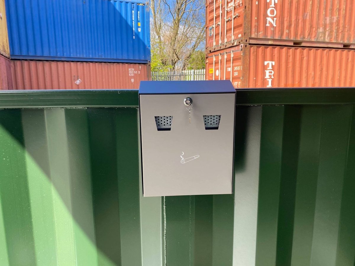 5ft × 8ft Steel Smoking Shelter – Ventilated, Lockable Enclosure – wall-mounted cigarette disposal bin on green corrugated shelter wall