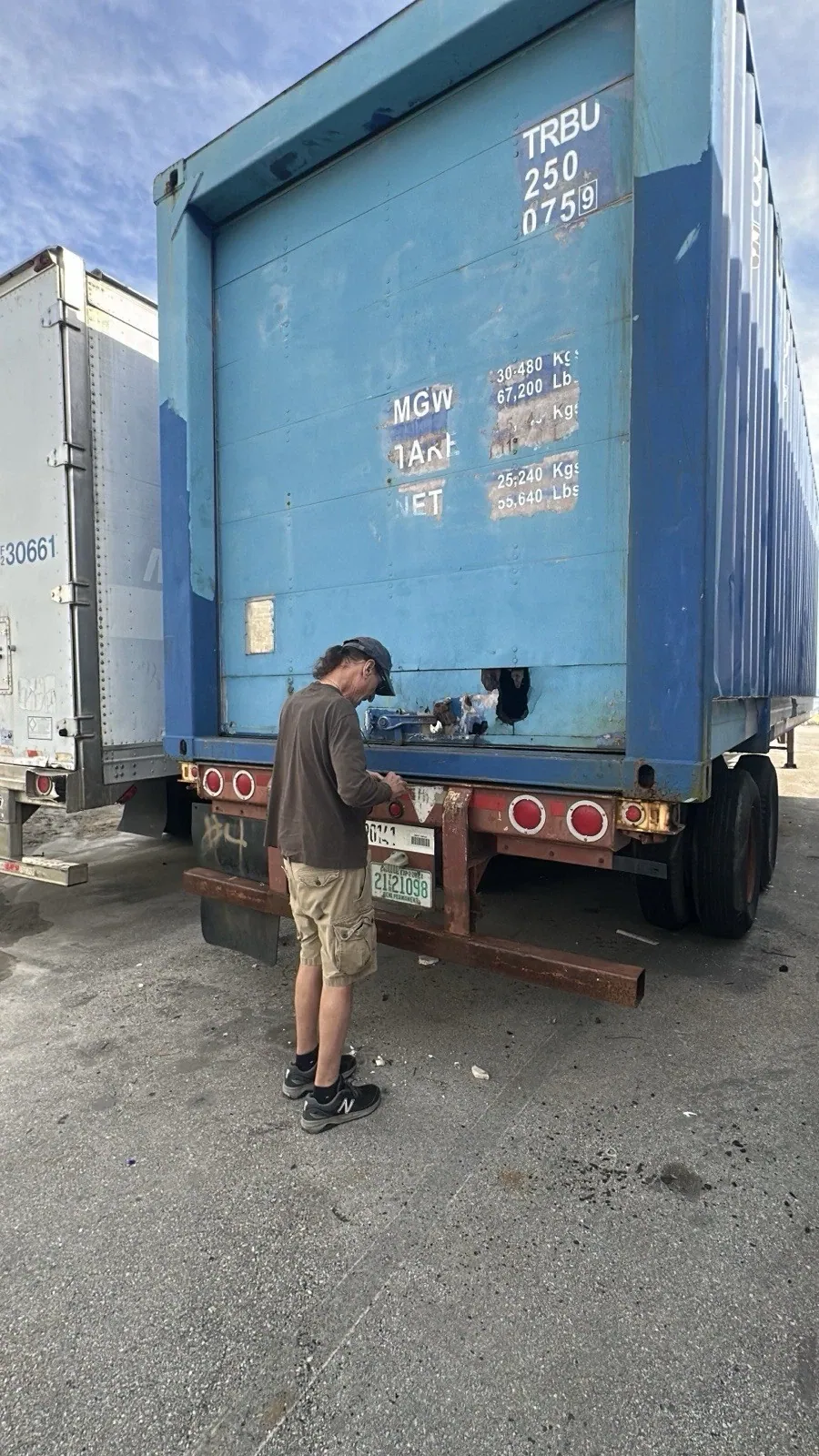 53ft High Cube Shipping Container – Used, Cargo Worthy – person inspecting damaged blue container end on trailer chassis