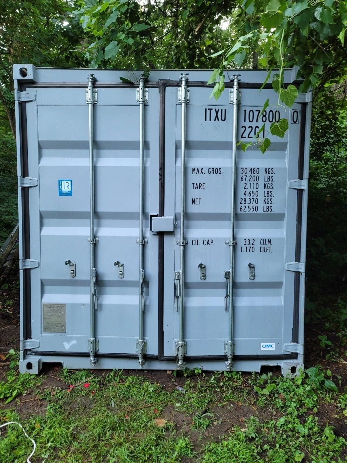 20ft Used Shipping Container – Wind & Watertight Storage – closed container cargo doors surrounded by trees and vegetation