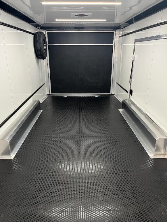 2026 ATC 24 ft ROM 550 Trailer – Black, Lithium – Interior view facing the rear ramp door with a spare tire mounted on the wall