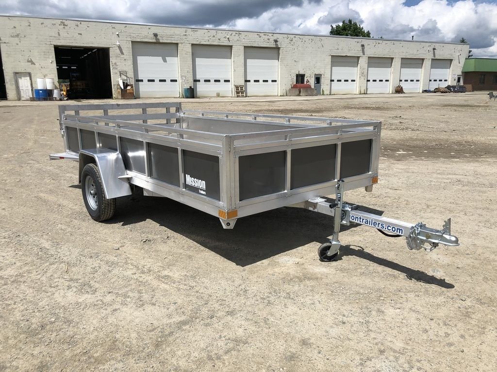 2022 Mission 6 × 12 ft Utility Trailer – Rear Ramp – Three-quarter front view of an aluminum utility trailer with grey side panels on dirt ground