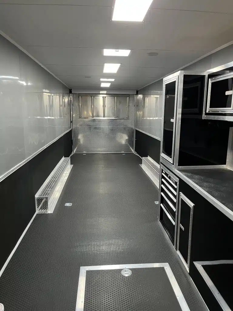 2025 Millennium 34 ft Car Hauler – Corner Bathroom – Interior view showing cabinets and tool drawers with coin flooring and bright lighting