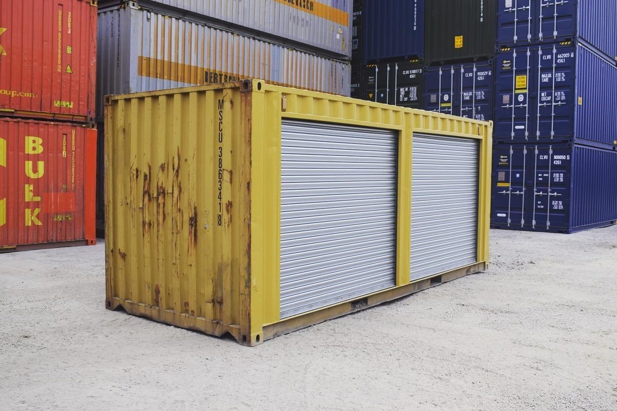 20ft Used Storage Container – Dual Side Roll-Up Doors – Weathered yellow storage container with two closed silver roll-up doors in a container yard