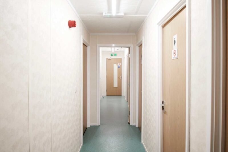 32 × 30 ft Modular Office – Green, 3 Bay – Narrow white hallway with multiple wooden doors and green flooring
