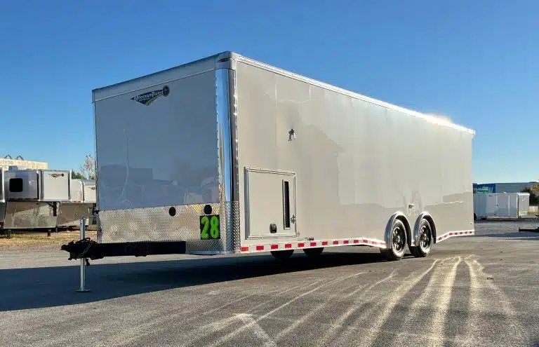 2026 Millennium 28 ft Car Hauler – White – Driver side and front view showing exterior storage compartment and spread axles