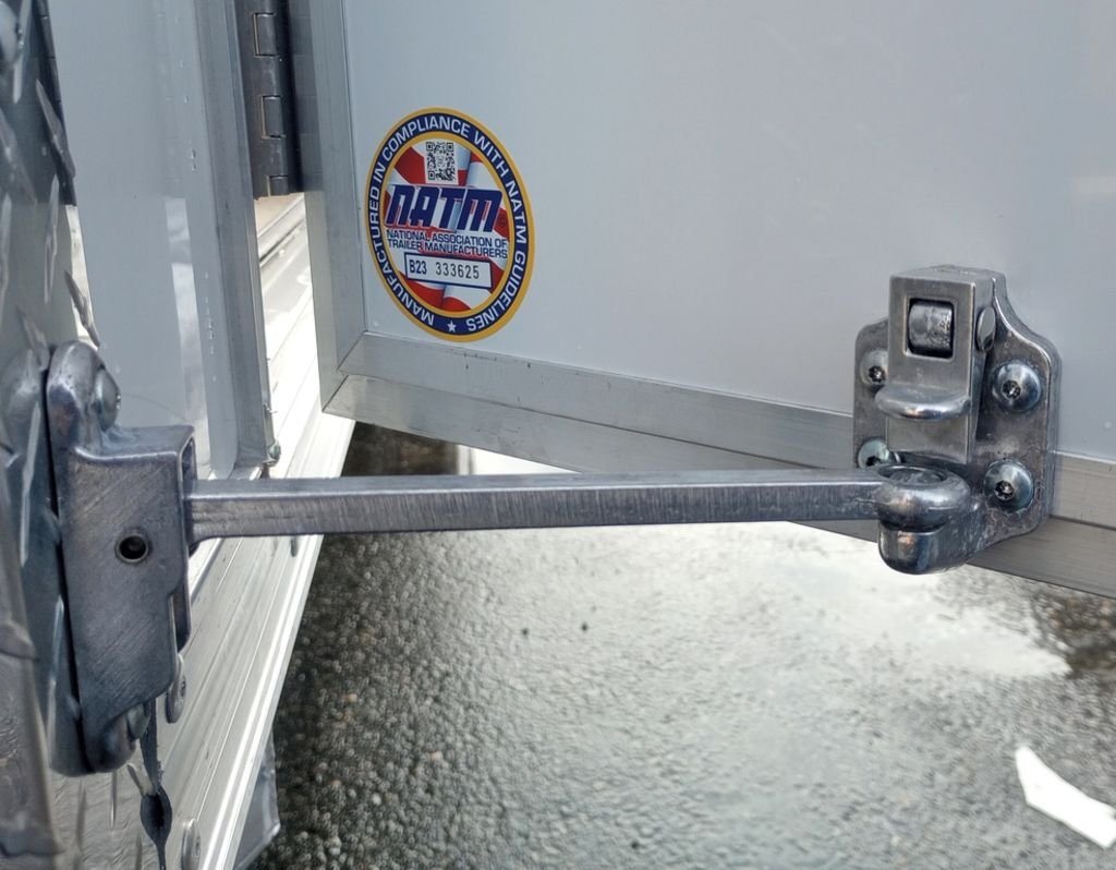2024 Mission Trailers 24 ft Deckover – Galvanized Package – Close-up of the trailer door latch and hinges with safety certification sticker