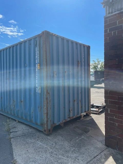 40ft High Cube Shipping Container – Used, Locking Doors – angled exterior view of weathered container beside brick building