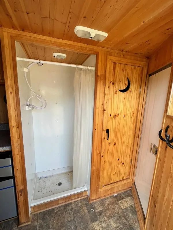 2004 Sundowner 3 Horse Trailer – Weekender Living Quarters – View of the interior shower stall next to a wood door with crescent cutout