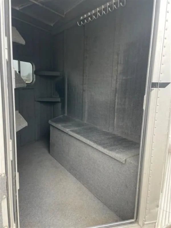 1999 Elite Custom 3 Horse Trailer – Rotating Saddle Rack – Interior of the tack room with carpeted walls and a storage bench
