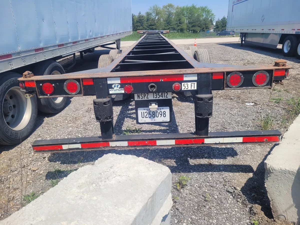 53ft Used Container Chassis – 2011, Spring Suspension – rear view of empty container chassis between parked trailers