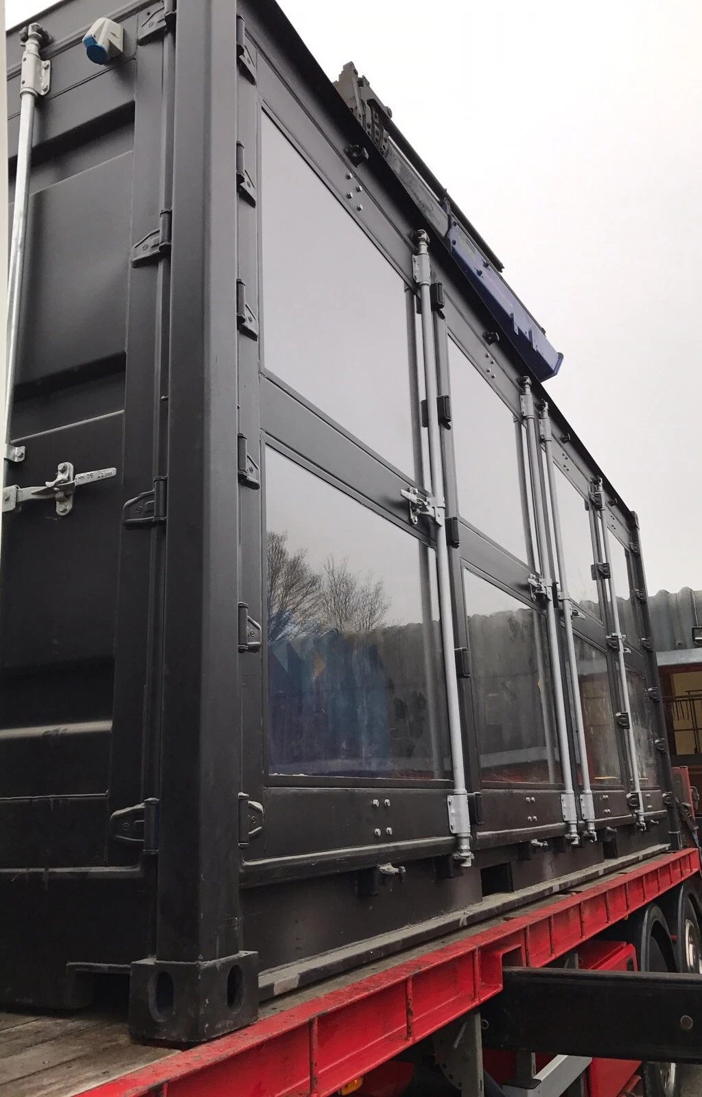 20ft Used Shipping Container – Integrated Glass Windows – low-angle exterior of glass-panel container on red flatbed trailer