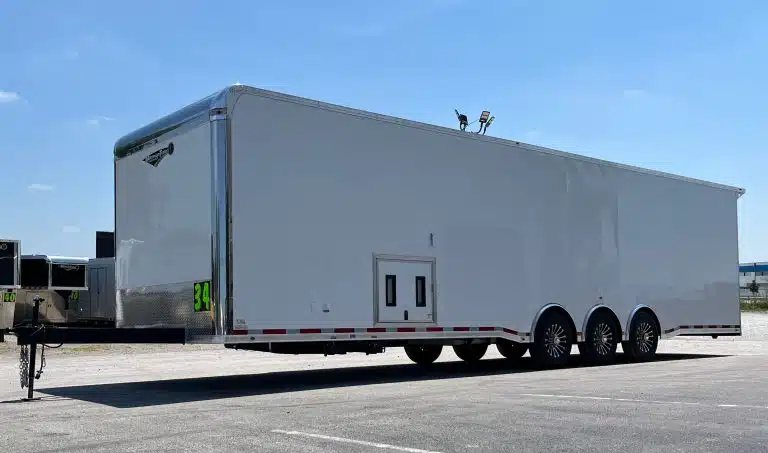 2025 Millennium 34 ft Car Hauler – Corner Bathroom – Full profile view of a large white enclosed trailer with triple axles and hitch