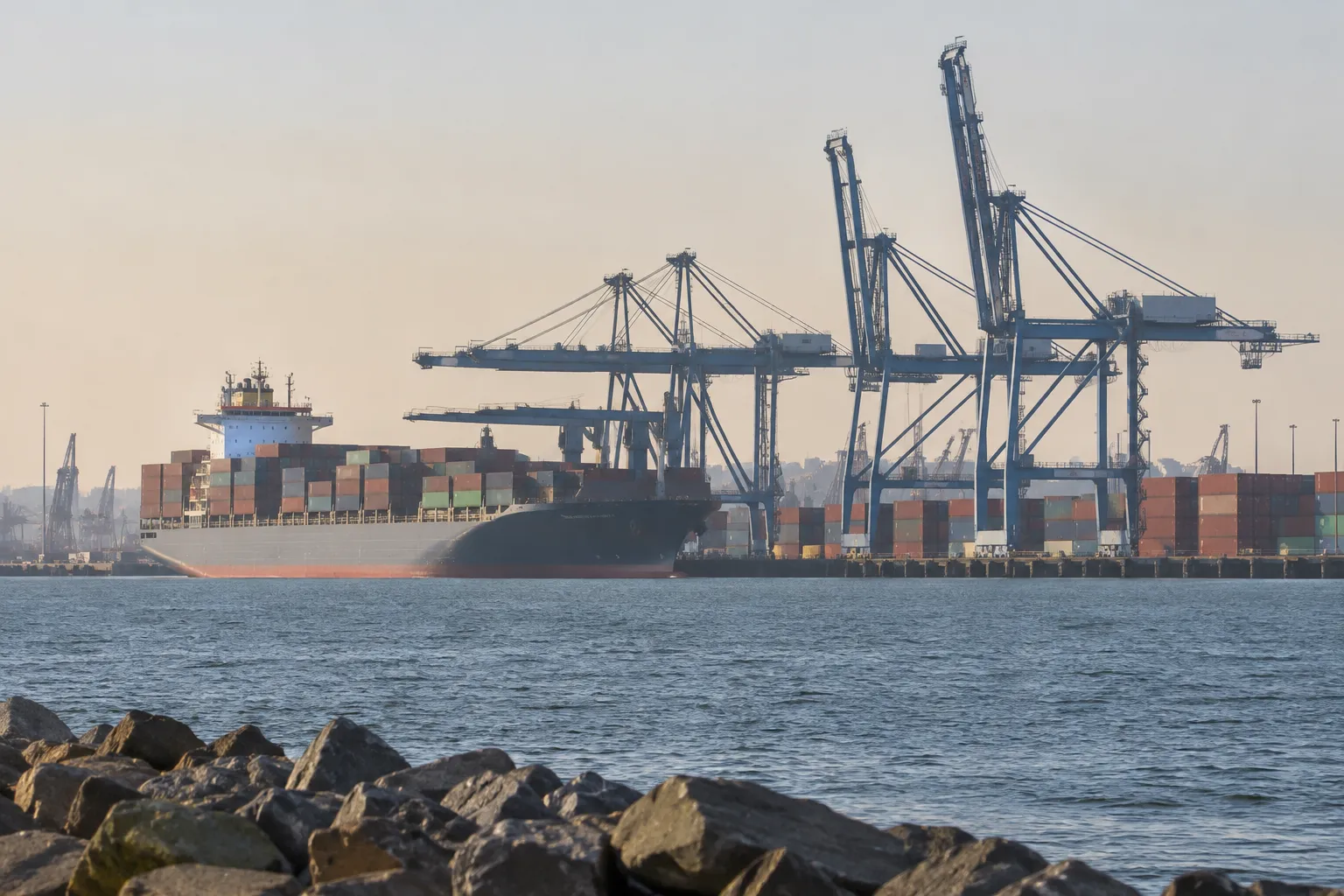 Port cranes and container vessel illustrate maritime activity behind shipping container tariffs 2026.